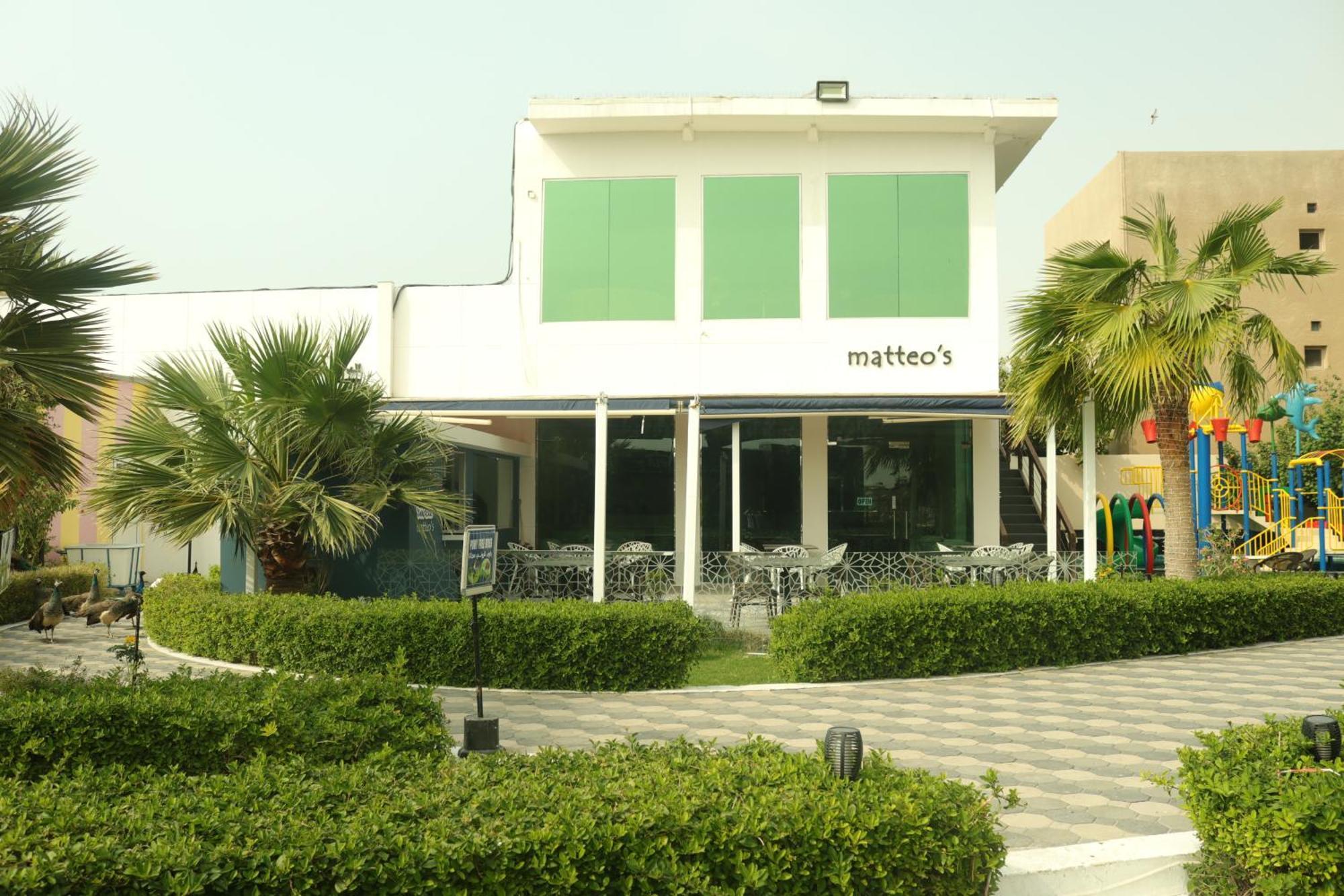 Lagoona Beach Luxury Resort And Spa Manama Ngoại thất bức ảnh The photo shows a building with the name "matteo's" displayed prominently on the front. The structure features large windows and green shutters. There is a landscaped area in front with bushes and palm trees, along with a paved pathway leading up to 