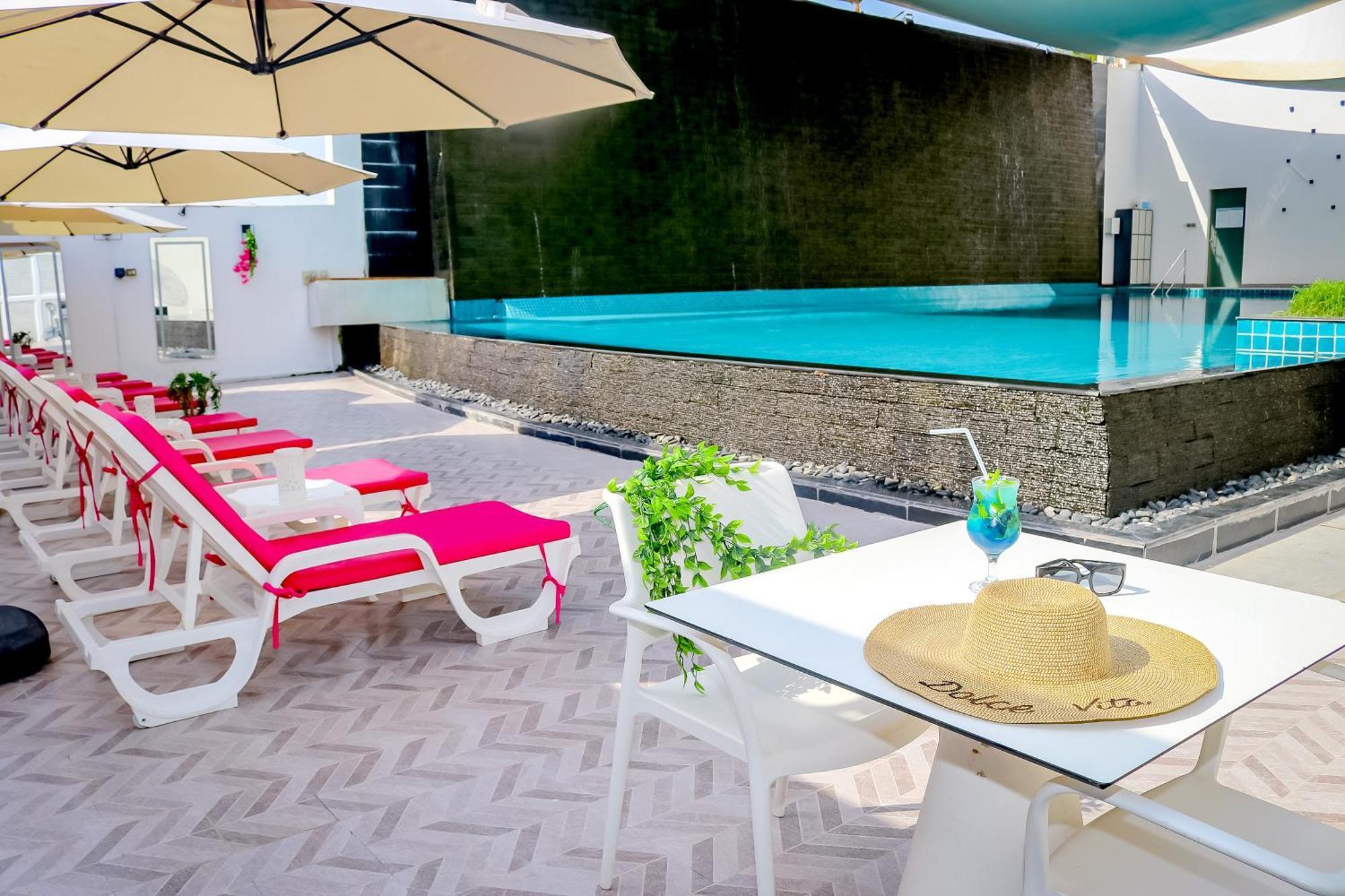 Lagoona Beach Luxury Resort And Spa Manama Ngoại thất bức ảnh The photo shows a sunny poolside area with bright red lounge chairs arranged neatly beside a swimming pool. There are large beige umbrellas providing shade. A small table is set up with a straw hat and a colorful drink, suggesting a relaxed, tropical