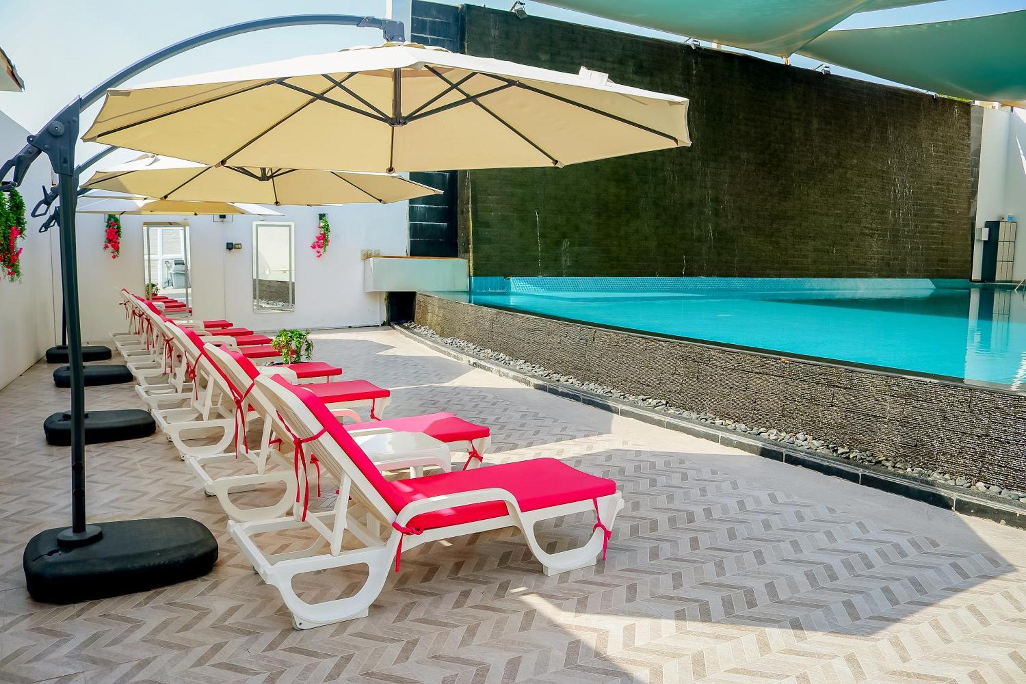 Lagoona Beach Luxury Resort And Spa Manama Ngoại thất bức ảnh The photo shows a sunny poolside area with several lounge chairs arranged in a row. Each chair features red cushions and is positioned under large, beige umbrellas for shade. In the background, there is a beautiful swimming pool with clear blue water