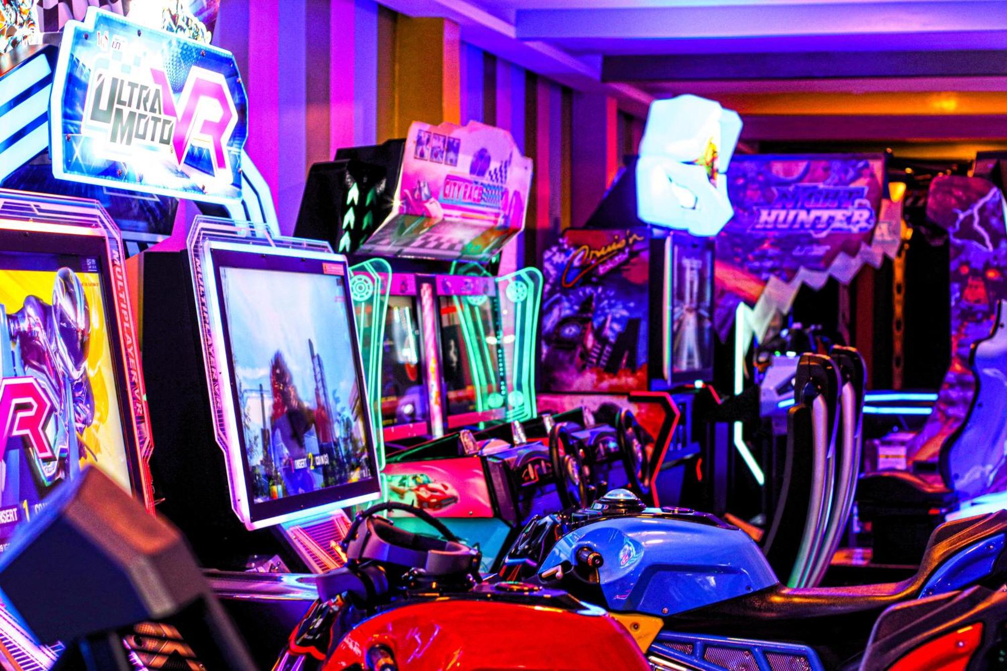 Lagoona Beach Luxury Resort And Spa Manama Ngoại thất bức ảnh The photo shows a vibrant arcade scene featuring various arcade gaming machines. The machines are lined up, showcasing colorful screens and bright, neon lights, creating an energetic atmosphere. Some machines appear to be racing games, as indicated b