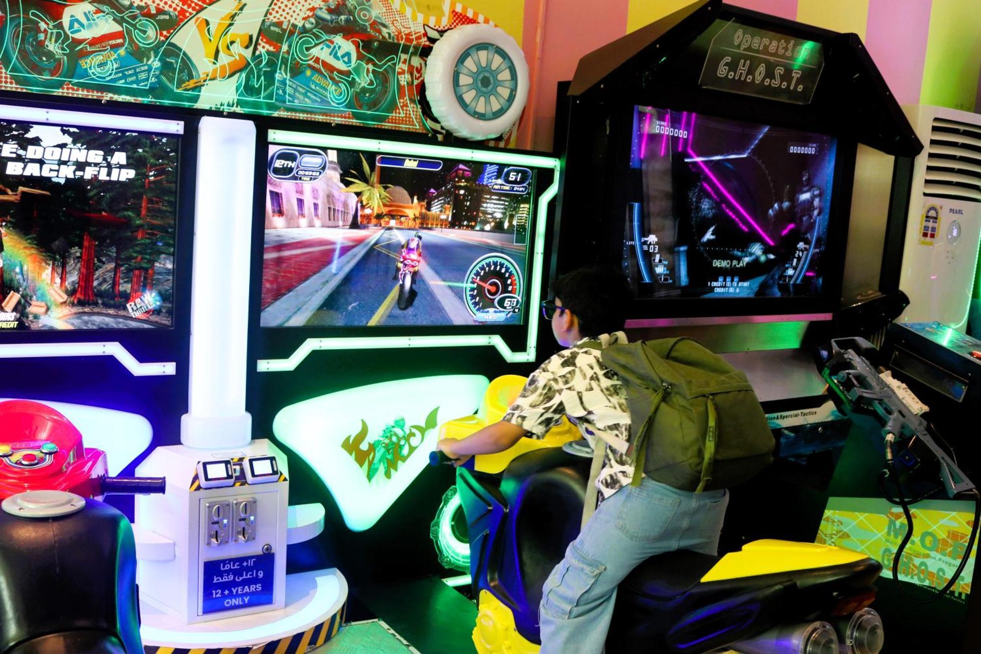 Lagoona Beach Luxury Resort And Spa Manama Ngoại thất bức ảnh The photo shows a person playing an arcade motorcycle racing game. They are seated on a motorcycle-shaped seat, actively engaging with the game displayed on the screen in front of them. The screen shows a vibrant racing scene with streets and colorfu
