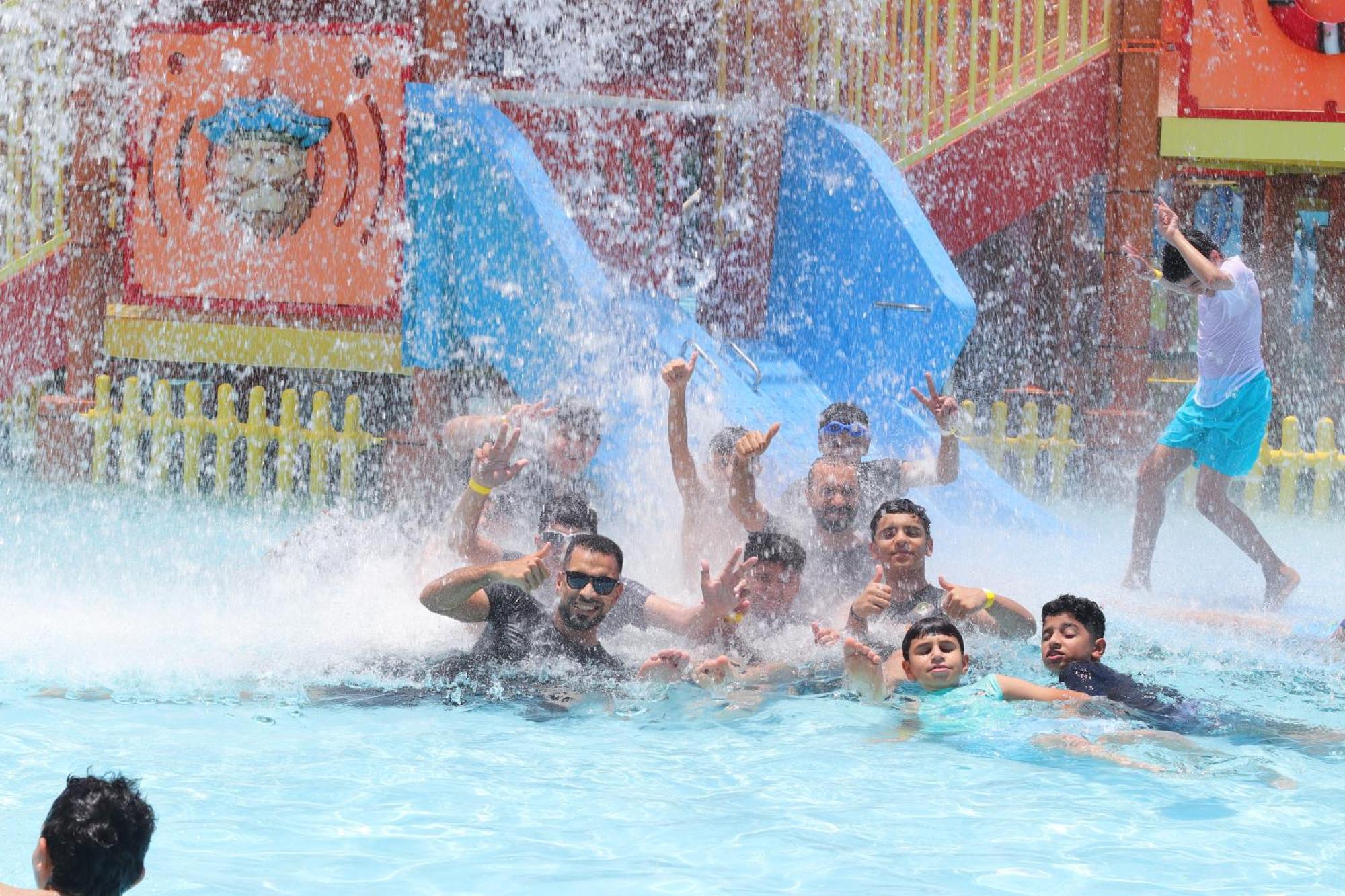 Lagoona Beach Luxury Resort And Spa Manama Ngoại thất bức ảnh The photo shows a lively scene at a water park or pool area. Several people, including adults and children, are enjoying themselves in the water, splashing and posing for the camera. Water is cascading down, creating a refreshing atmosphere. In the b