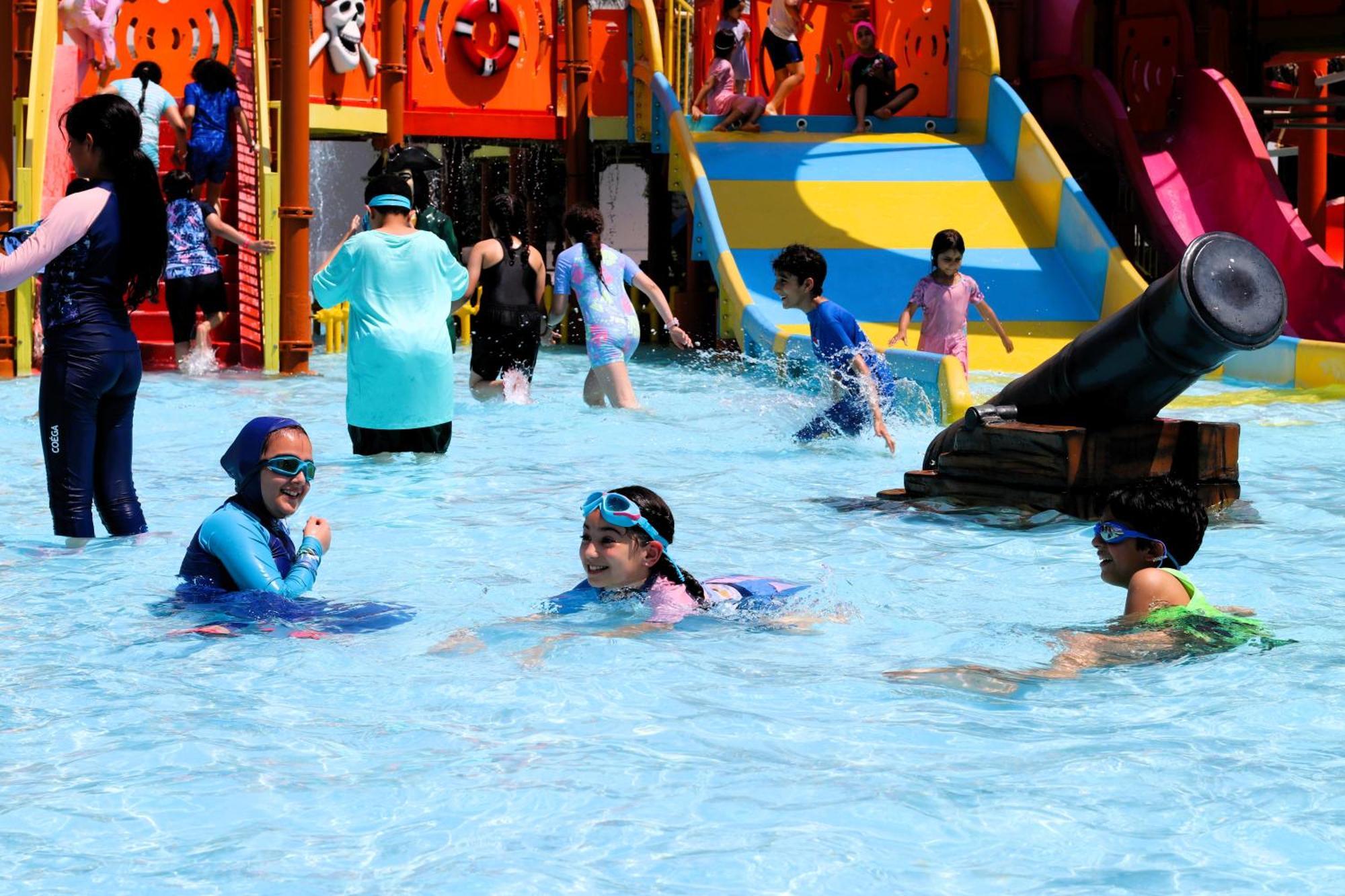 Lagoona Beach Luxury Resort And Spa Manama Ngoại thất bức ảnh The photo shows a vibrant water park scene with several children playing in a shallow pool. Some are swimming and splashing around, while others are playing on colorful slides in the background. The atmosphere is lively and cheerful, with kids of var