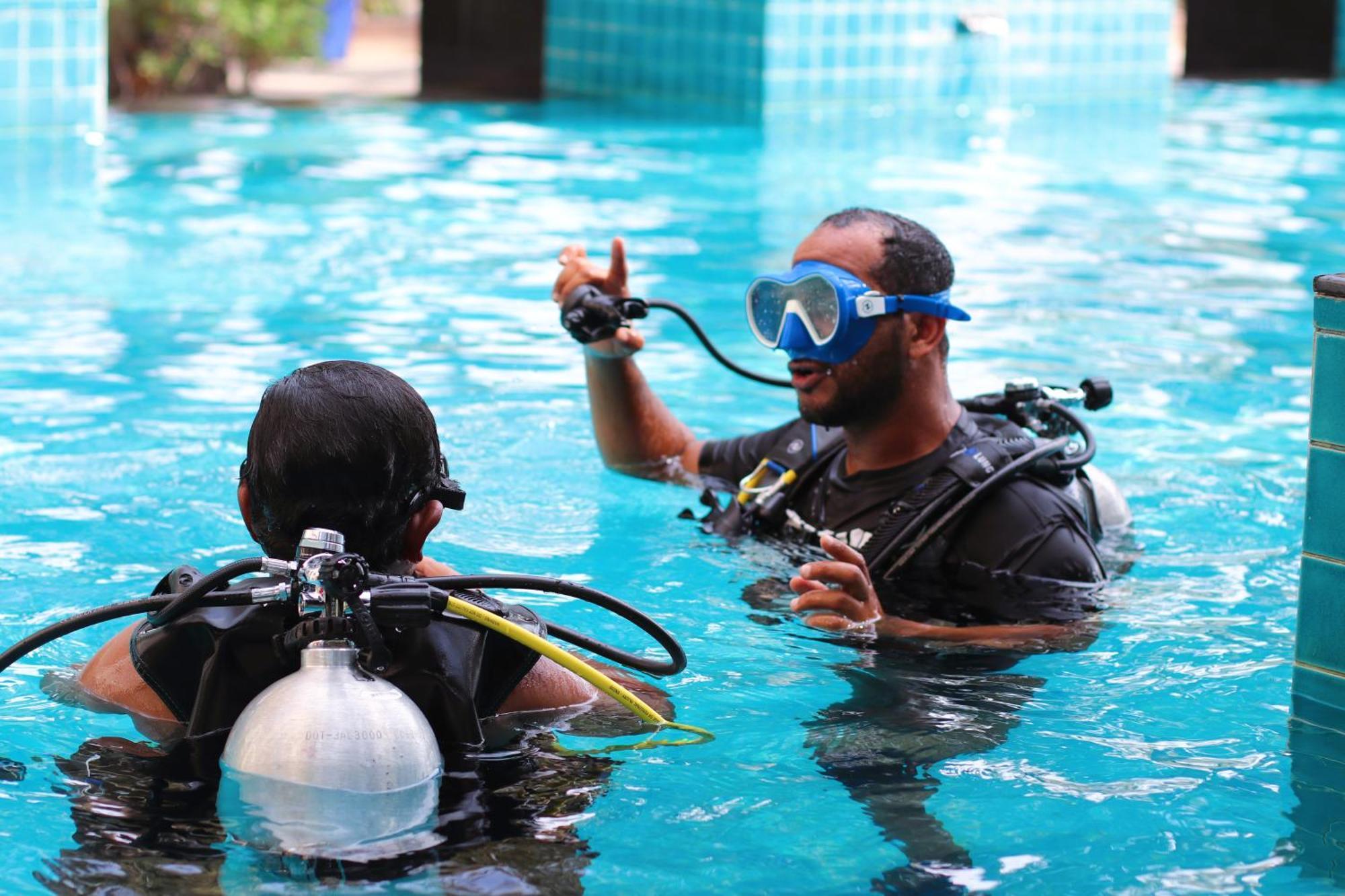 Lagoona Beach Luxury Resort And Spa Manama Ngoại thất bức ảnh The photo shows two divers in a pool. One diver is wearing a scuba mask and is speaking to the other diver, who is also equipped with scuba gear. They appear to be engaged in a discussion, possibly related to diving instructions or safety. The water 