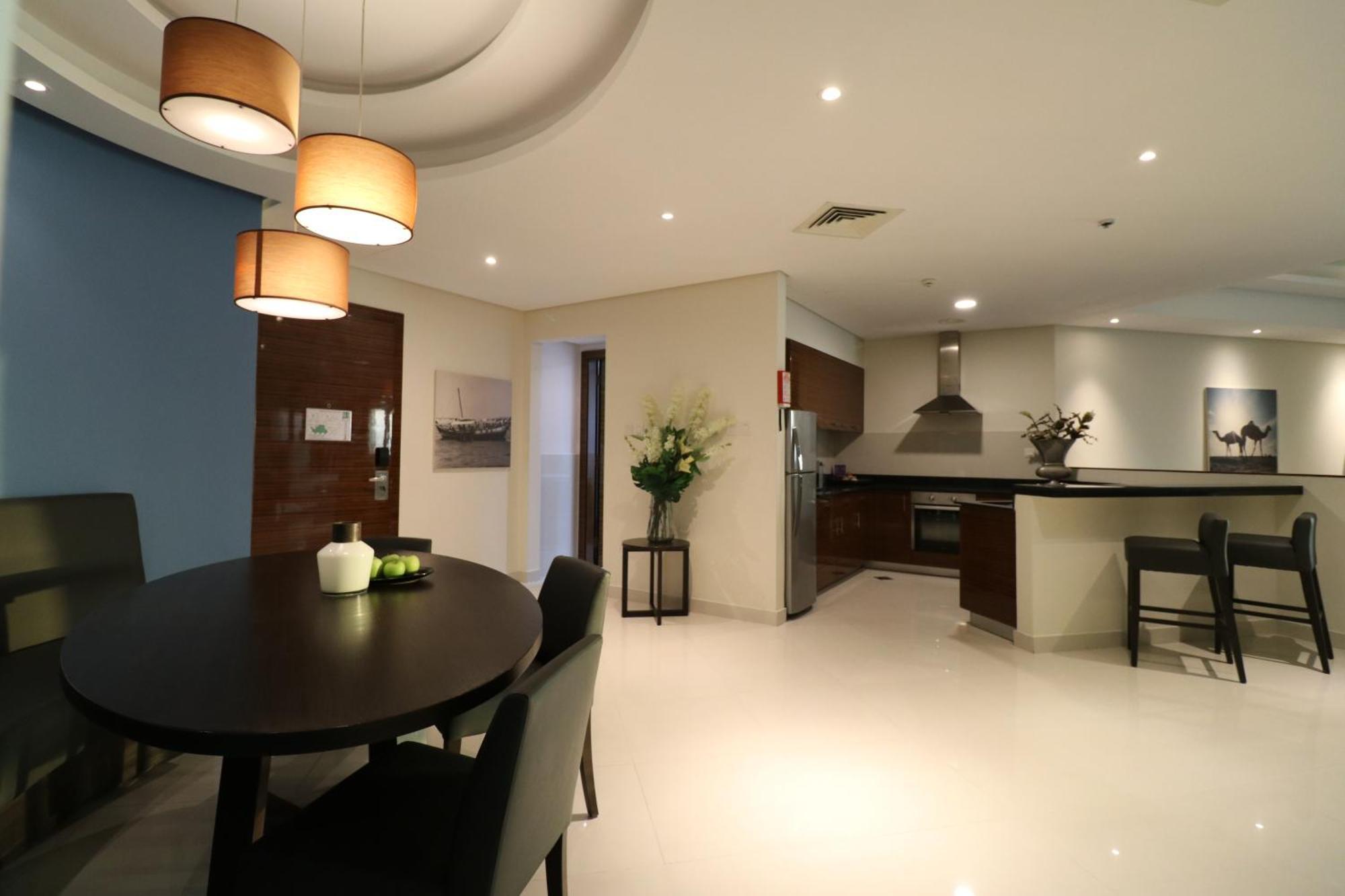 Lagoona Beach Luxury Resort And Spa Manama Ngoại thất bức ảnh The photo shows a modern, open-concept dining and kitchen area. On the left, there is a round dining table with black chairs, accompanied by a few decorative elements like a small vase and some fruit. The walls have a combination of light and dark to