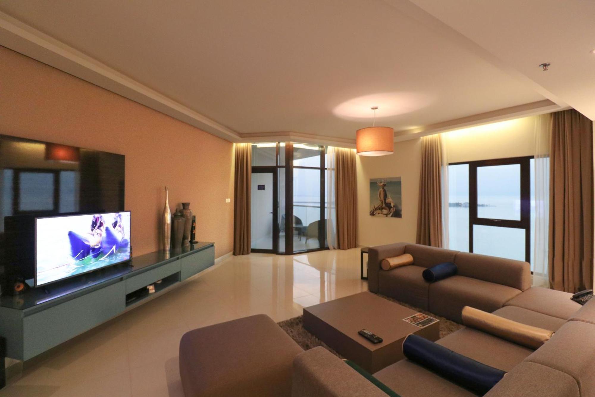 Lagoona Beach Luxury Resort And Spa Manama Ngoại thất bức ảnh The photo shows a modern living room with a sleek design. There is a large wall-mounted television on a contemporary entertainment unit, with decorative items placed beside it. The room features a comfortable sectional sofa in light tones, with a cof